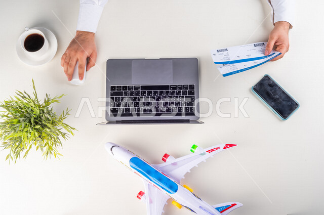 A close-up from the top, of a Saudi Arabian Gulf man putting flight ticket information on his laptop at the airport, working environment, white background