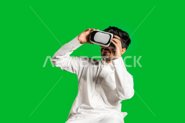 Chroma, a happy Saudi Gulf man, puts the VR Box, face and hand gestures indicating happiness and enjoyment, the use of 3D technology, green background