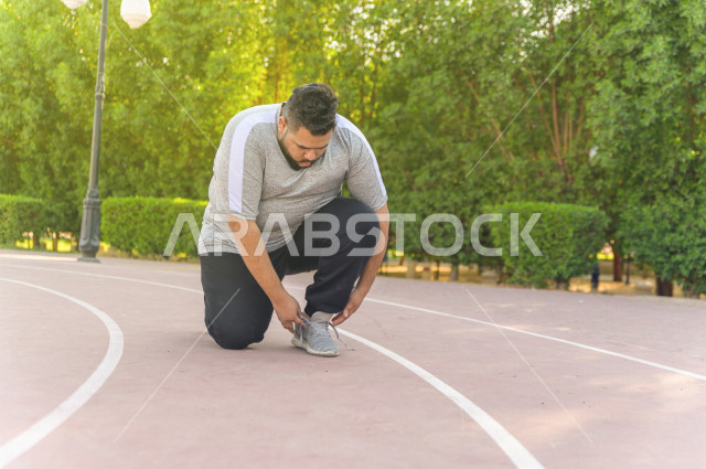 رجل شاب سعودي خليجي  يقوم بالاستعداد لممارسة الرياضة الصباحية في الهواء الطلق ،ممارسة رياضة المشي ، ممارسة الرياضة على طريق الممشى المخصص للمشي ، نشاط بدني  للمحافظة على اللياقة و الصحة الجيدة ، ممارسة التمارين الرياضية 