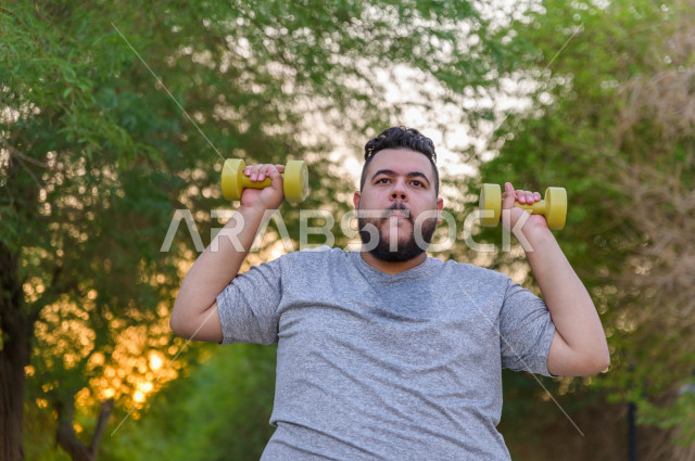 شاب سعودي خليجي سمين  يمارس الرياضة  في الهواء الطلق ، يحمل اوزان و اثقال ، يعاني من السمنة ، مشاكل صحية ،الوزن الزائد والسمنة ، خسارة السعرات الحرارية  ، نشاط بدني  للمحافظة على اللياقة و الصحة الجيدة ، ممارسة التمارين الرياضية 