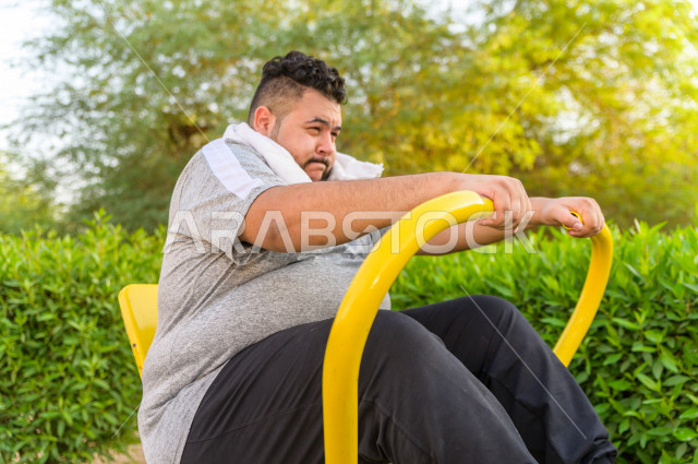 شاب سعودي خليجي يعاني من السمنة الزائدة ، يمارس الرياضة الصباحية في الهواء الطلق ، يمارس الرياضة على اجهزة الكترونية  ، نشاط بدني  للمحافظة على اللياقة و الصحة الجيدة ، ممارسة التمارين الرياضية