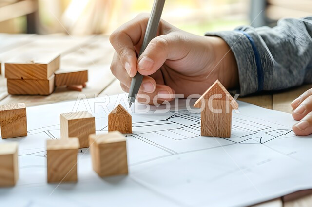 وظائف ومهن هندسية مستقبلية، قياس المسافات ورسم الخطوط المستقيمة بقلم الرصاص، صورة مقربة ليد شاب عربي خليجي سعودي يقوم بانجاز الواجب الجامعي وبجانبه اشكال على شكل بيوت خشبية، الدراسة في مجال الهندسة المعمارية