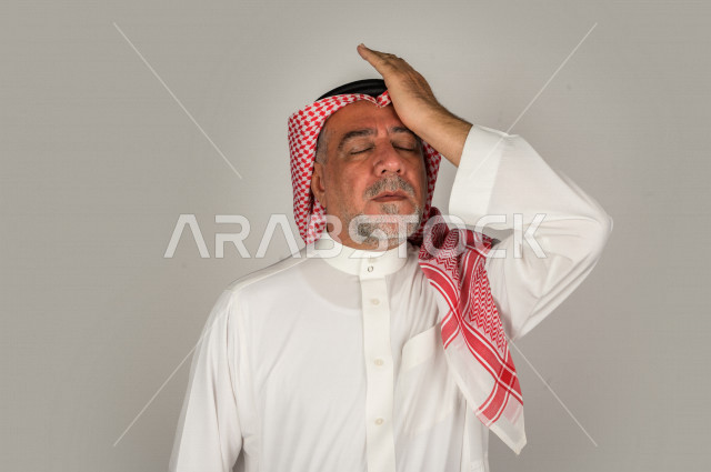 بورتريه لرجل كبير بالسن سعودي خليجي  مريض بإيماءات الوجه و اليدين التي تدل على الألم والمعاناه،  تعابير وجه ، خلفية بيضاء