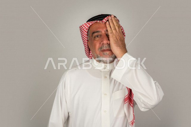 بورتريه لرجل كبير بالسن سعودي خليجي  مريض بإيماءات الوجه و اليدين التي تدل على الألم والمعاناه،  تعابير وجه ، خلفية بيضاء