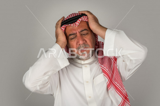Portrait of an elderly Saudi Gulf man who is sick with face and hand gestures indicating pain and suffering, facial expressions, white background