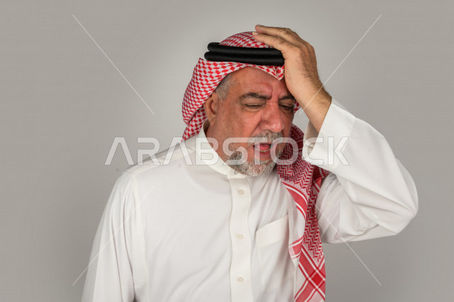 بورتريه لرجل كبير بالسن سعودي خليجي  مريض بإيماءات الوجه و اليدين التي تدل على الألم والمعاناه،  تعابير وجه ، خلفية بيضاء