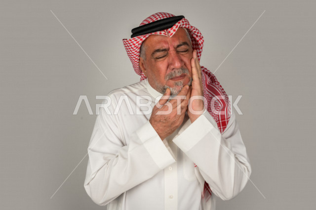 Portrait of an elderly Saudi Gulf man who is sick with face and hand gestures indicating pain and suffering, facial expressions, white background