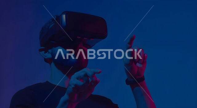 التفاعل ومحاكاة العالم الخيالي، بورتريه مقرب لرجل عربي خليجي سعودي يقوم بالنقر والإشارة الى شيء ما، مشاهدة أفلام عبر نظارات الواقع الإفتراضي، الأجهزة والتقنيات الحديثة والمتطورة، لعب ألعاب الفيديو ثلاثية الأبعاد، خلفية زرقاء