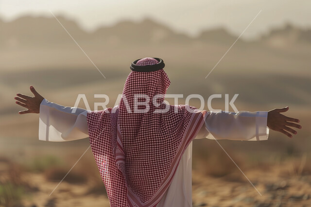 تعابير الترحيب والاستقبال، صورة من الخلف لرجل عربي خليجي سعودي يرتدي الشماغ والثوب التقليدي يرفع يديه للاعلى يقف باستقامة في المناطق الصحراوية، الشعور بالفرح والسرور، الاهتمام بالأناقة والمظهر الخارجي