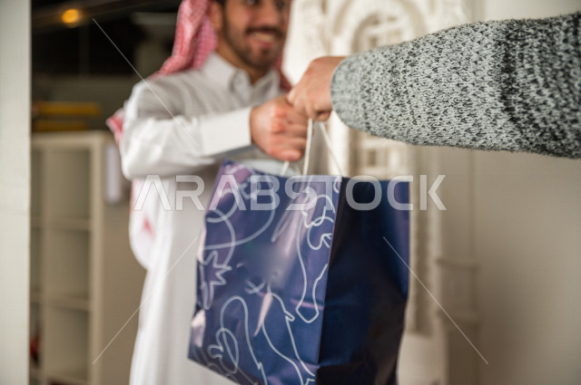 رجل سعودي يستلم طلبه من أمام الباب , وجبات صحية مفيدة , توصيل الطلبات . 