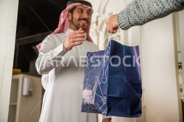 A Saudi man receives his order in front of the door, wholesome, useful meals, delivery of orders.