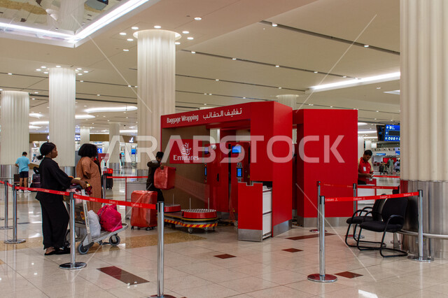 ماكينة تغليف الحقائب, خدمة تغليف الأمتعة، الخدمات المميزة داخل المطار، المسافرون ينتظرون في الطابور في مطار دبي الدولي في الإمارات العربية المتحدة، أماكن و معالم سياحية مشهورة, مفهوم السياحة و السفر