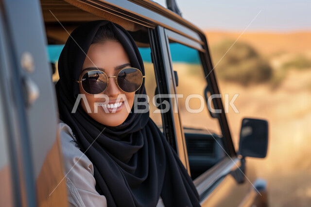 الخروج في نزهة الى المناطق الصحراوية في المملكة العربية السعودية، وسائل النقل الآمنة، صورة مقربة لامرأة عربية خليجية سعودية محجبة ترتدي نظارة شمسية تخرج رأسها من نافذة السيارة، الاستمتاع بالإجازات والعطلات الصيفية