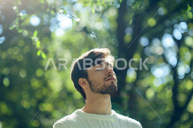 التأمل والاستجمام والشعور بالراحة، استنشاق الهواء الطلق عبر المشي و التنزه في الحدائق العامة، تعابير التخيل وتذكر شيء ما،  صورة مقربة لشاب عربي خليجي سعودي مبتسم يغمض عينيه، الطبيعة الخضراء في المملكة العربية السعودية، قضاء أوقات ممتعة في العطلة الصيفية