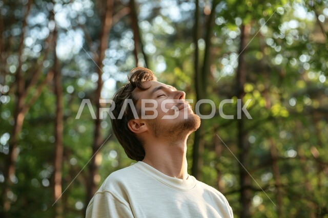 قضاء أوقات ممتعة في العطلة الصيفية، الشعور بالراحة والتأمل والاستجمام، المشي و التنزه في الحدائق العامة لاستنشاق الهواء الطلق ، صورة مقربة لشاب عربي خليجي سعودي مبتسم يغمض عينيه بايماءات التخيل، الطبيعة الخضراء في المملكة العربية السعودية