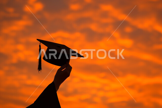 Education in the Kingdom of Saudi Arabia, the concept of diligence and excellence, a silhouette of the hand of a student wearing an abaya holding a graduation cap and raising it up at sunset, a feeling of pride and self-confidence, celebrating the completion of university studies, cellulite