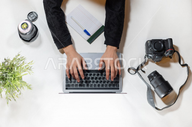  تصوير مقرب من الأعلى , لمصورة عربية سعودية لديها خبره في التقاط الصور , مصورة فوتوجرافيا تدخل الصور من خلال اللابتوب على مكتب أبيض , وظيفه ومهن , بيئة عمل , خلفية بيضاء .