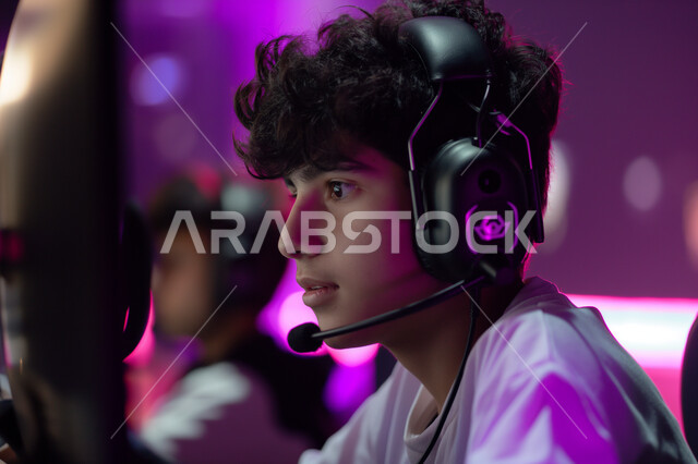 Entertaining and enjoying video games in free time, a young Saudi Arab Gulf teenager wearing headphones playing PlayStation, gestures and expressions for integration and interaction with the game, technical and technological development of modern devices, enjoyable entertainment activities