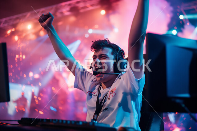 Happiness and enthusiasm for winning, enjoyable recreational activities, technical and technological development of modern devices, entertainment and enjoyment with video games in free time, a young Saudi Arabian Gulf teenager wearing headphones playing PlayStation