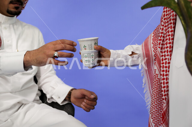 الاستمتاع بالمشروبات الساخنة، اتباع العادات والتقاليد السعودية في تقديم القهوة العربية بالدله النحاسية والفنجان، حسن الضيافه والإستقبال في الأعياد والمناسبات الدينية، منتجات وطنية محلية،  صورة مقربة ليد رجل عربي حليجي يرتدي الثوب التقليدي والشماغ يقوم بصب القهوة