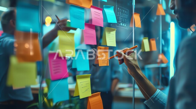 كتابة الاهداف المستقبيله والافكار الجديده والذكيه، صورة مقربة ليدي شاب عربي خليجي سعودي يقومان بتدوين الملاحظات والمهام، توزيع الاعمال المطلوبه، نوتات ملونه معلقه على الجدران