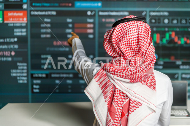 رجل سعودي خليجي يعمل في قسم التحليلات الرقمية  ، يقوم بتتبع الأرقام و تحليلها و دراستها  ، يرتدي الزي السعودي التقليدي