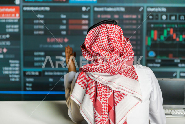 رجل سعودي خليجي يعمل في قسم التحليلات الرقمية  ، يقوم بتتبع الأرقام و تحليلها و دراستها  ، يرتدي الزي السعودي التقليدي