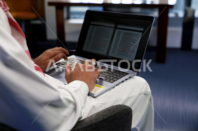 استخدام الأجهزة التكنولوجية الحديثة والمتطورة، شركات ومكاتب في المملكة العربية السعودية، تنظيم شؤون الأعمال وإدارتها، وظائف ومهن ادارية مكتبية, موظف عربي خليجي سعودي يرتدي الثوب التقليدي يقوم بالعمل على الحاسوب داخل المكتب