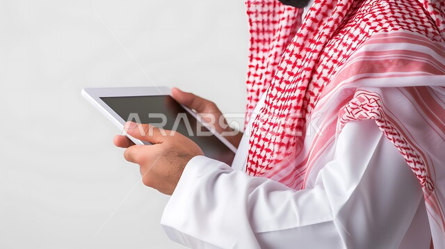 استخدام الأجهزة والتقنيات الحديثة, التواصل مع الاصدقاء عبر الانترنت, متابعه آخر أخبار السوشال ميديا, بورتريه مقرب لرجل عربي خليجي سعودي يرتدي الثوب التقليدي والشماغ يقوم بحمل جهاز التابليت, خلفية بيضاء