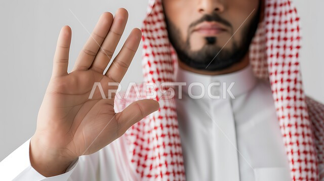 A request to stop and refrain from doing something, a close-up portrait of a Saudi Gulf Arab man wearing a shemagh and traditional dress, raising his hand up with a stop sign, gestures of concern and annoyance about something, non-acceptance and rejection, white background