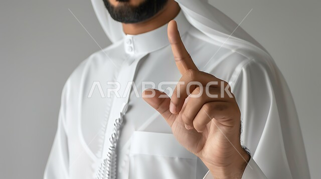 Pointing to something with gestures of identification and confirmation, close-up portrait of a Saudi Gulf Arab man wearing traditional clothing, pointing with his index fingers with warning and warning expressions, gray background
