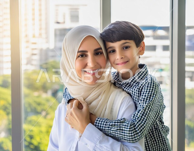 مفهوم الأمومة والطفولة، النظر الى الكاميرا بإيماءات السعادة والسرور، قضاء أوقات ممتعة مع الأولاد، تحمل المسؤوليه ودور الأسرة السعوديه في تربيه الأبناء, صورة مقربة لأم عربية سعودية خليجية محجبة تقوم باحتضان ابنها بحب