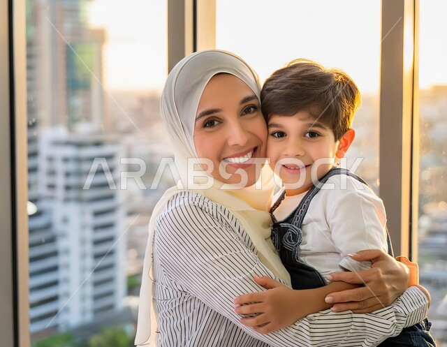  النظر الى الكاميرا بإيماءات السعادة والسرور، قضاء أوقات ممتعة مع الأولاد، تحمل المسؤوليه ودور الأسرة السعوديه في تربيه الأبناء, صورة مقربة لأم عربية سعودية خليجية محجبة تقوم باحتضان ابنها بحب، مفهوم الأمومة والطفولة