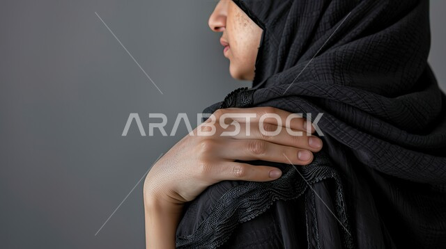 التهاب العضلات والمفاصل والحاجه للعلاج،  المعاناة من الآلام والأوجاع العصبية والعضلية، بورتريه مقرب من الخلف لإمرأة عربيه سعوديه خليجيه ترتدي العباءة والحجاب تضع يدها على كتفها  بإيماءات الألم والتعب والأرهاق, خلفية رمادية