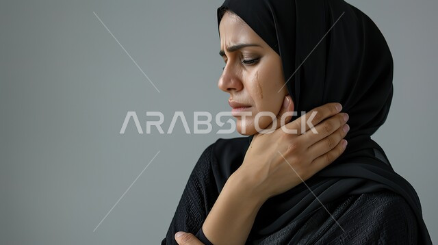 الحاجه للعلاج الفيزيائي، الإحساس بالتعب والإرهاق، مفهوم وجع مفاصل الرقبة، إيماءات مختلفة تدل على الشعور بالألم، بورتريه مقرب لإمرأة عربية سعودية خليجية محجبة ترتدي العباءة تضع يدها على رقبتها،طلب المساعده والحاجه للعلاج، خلفية رمادية