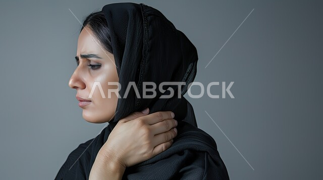 مفهوم وجع مفاصل الرقبة، الحاجه للعلاج الفيزيائي، الإحساس بالتعب والإرهاق، إيماءات مختلفة تدل على الشعور بالألم، بورتريه مقرب لإمرأة عربية سعودية خليجية محجبة ترتدي العباءة تضع يدها على رقبتها،طلب المساعده والحاجه للعلاج، خلفية رمادية