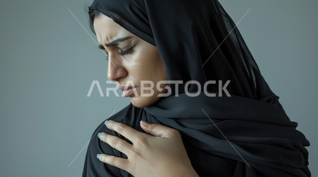 الأوجاع والآلام العصبية والعضلية، طلب المساعده والحاجه للعلاج، التهاب العضلات والمفاصل، بورتريه مقرب لإمرأة عربيه سعوديه خليجيه ترتدي العباءة والحجاب تضع يدها على كتفها بإيماءات الألم والتعب والأرهاق, خلفية رمادية