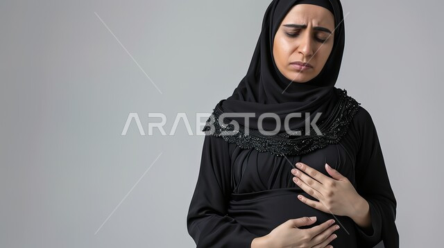 مشاكل صحية صعبة، الذبحه الصدريه حالة مرضية،طلب المساعده والحاجه للعلاج، إيماءات التعب والإرهاق والضغوطات النفسية، بورتريه مقرب لإمرأة عربية سعودية خليجية محجبة ترتدي العباءة تضع يدها على قلبها تشعر بحالة سيئة من الوخز والألم, خلفية رمادية