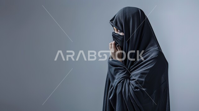 Feeling tired and sick, being infected with the Corona virus Covid-19, a close-up portrait from the side of a veiled Saudi Gulf Arab woman wearing a black abaya, facial and hand gestures indicating sneezing, gray background