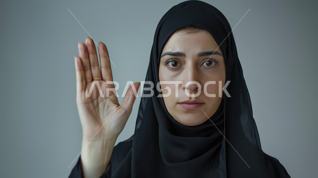 الأمر بالتوقف عن فعل شيء ما، تعابير الرفض والإمتناع، بورتريه مقرب لامرأه عربيه خليجيه سعوديه محجة ترتدي عباءة سوداء ترفع يدها بإيماءات تدل على النهي، الشعور بالإنزعاج والغضب، خلفية رمادية