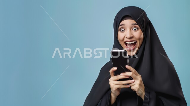 استخدام الاجهزة التكنولوجية الحديثة، سماع الاخبار والمفاجأت السعيدة، ايماءات الدهشة والسرور، بورتريه لإمرأة عربية خليجية سعودية محجبة مبتسمة تنظر إلى هاتفها المحمول بتعابير الفرح والسعادة، الدردشة والتواصل مع الاهل والاصدقاء، خلفية زرقاء