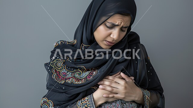حرقة في المعدة وعسر الهضم، الشعور بالشعور بآلام المخاض  وقرب الولاده، الإرهاق والتعب والإحساس بالمغص، بورتريه مقرب لإمرأة عربية سعودية خليجية محجبة حامل ترتدي العباءة تمسك بطنها بإيماءات الشعور بالألم، الحاجة لوضع خطة علاجية، خلفية رمادية