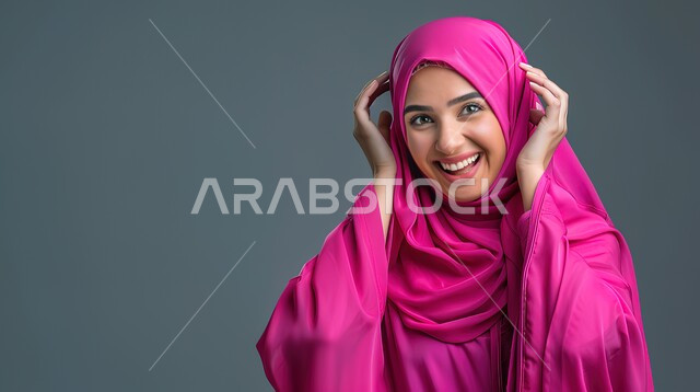 السعادة والسرور لسماع الأخبار السارة، الدهشة لحدوث أمر ما، تعابير المفاجأة والذهول, بورتريه مقرب لإمرأة عربية سعودية خليجية محجبة مبتسمة تضع يديها على رأسها بايماءات الاستغراب, خلفية رمادية 