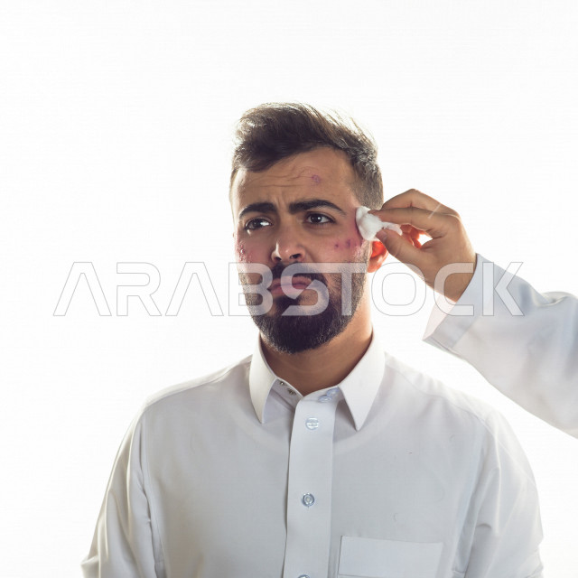 بورتريه لرجل سعودي خليجي مصاب بعدة مشاكل في منطقة الوجه، التعرض للحروق ،  بثور وجه منتشرة على البشرة ، ايماءات و تعبيرات وجه و يدين تدل على الآلم و الحزن ، مشاكل صحية و اصابات جسدية ، خلفية بيضاء