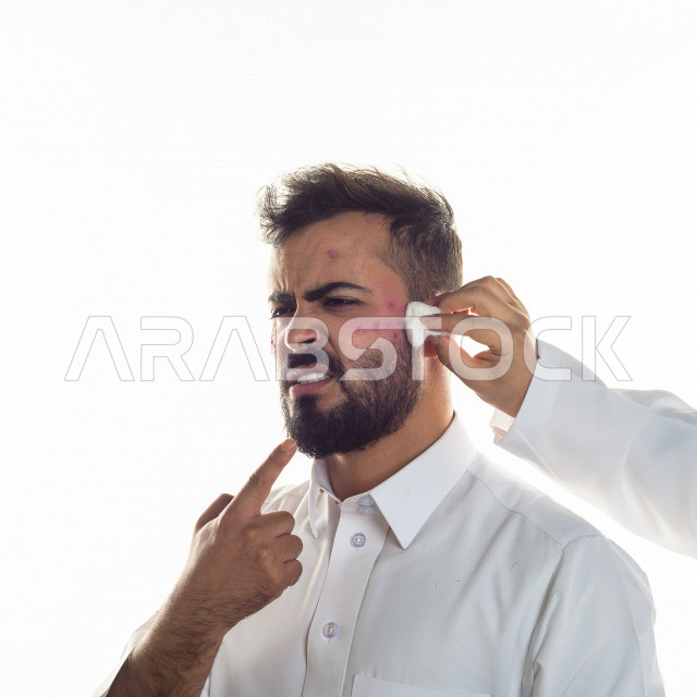 بورتريه لرجل سعودي خليجي مصاب بعدة مشاكل في منطقة الوجه، التعرض للحروق ،  بثور وجه منتشرة على البشرة ، ايماءات و تعبيرات وجه و يدين تدل على الآلم و الحزن ، مشاكل صحية و اصابات جسدية ، خلفية بيضاء