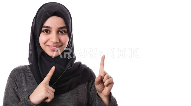 إشارات وحركات يدين تدل على هذا المكان (هنا)، تحديد موقع معين بإيماءات البشاشة، بورتريه مقرب لامرأة عربيه خليجيه سعوديه مبتسمه محجبه ترفع اصابعها السبابة وتشير الى شيء ما، خلفية بيضاء