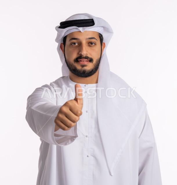 النظر إلى الكاميرا بتعابير الإعجاب والرضا، مفهوم الجودة والامتياز، بورتريه مقرب لرجل عربي خليجي إماراتي يرتدي الكندورة الإماراتية مع الغترة البيضاء يرفع يده بإيماءات القبول والموافقة، خلفيه بيضاء