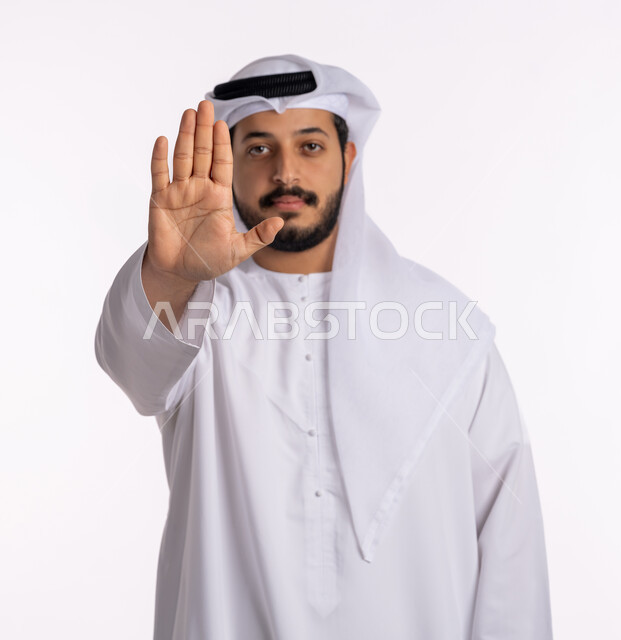 النظر إلى الكاميرا بتعابير الحزم والجدية، طلب المنع والتوقف عن فعل شيء ما، بورتريه لرجل عربي خليجي إماراتي يرتدي الكندورة والغترة يرفع يده بإيماءات الرفض والامتناع، خلفية بيضاء