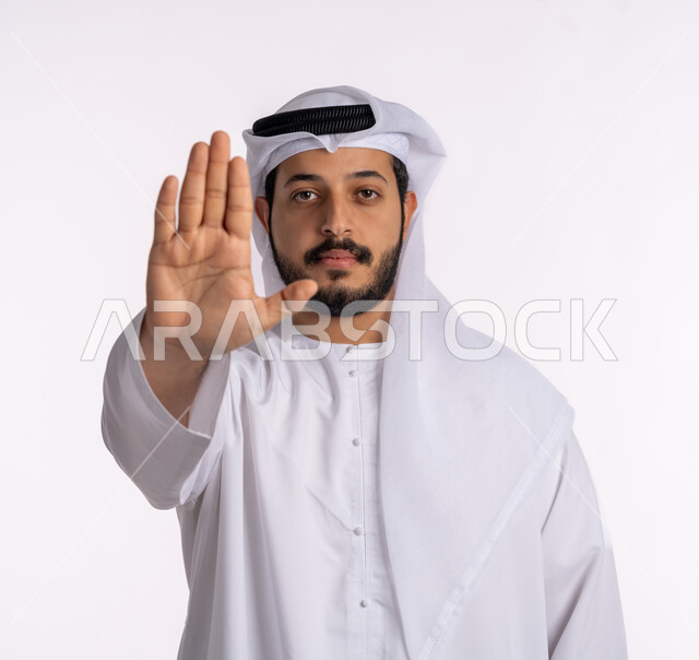 إيماءات الرفض والامتناع، طلب المنع والتوقف عن فعل شيء ما، بورتريه مقرب لرجل عربي خليجي إماراتي يرتدي الكندورة والغترة ينظر إلى الكاميرا بتعابير الحزم والجدية، خلفية بيضاء