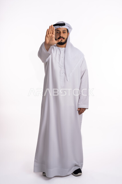 طلب المنع والتوقف عن فعل شيء ما، إيماءات الرفض والامتناع، بورتريه لرجل عربي خليجي إماراتي يرتدي الكندورة والغترة ينظر إلى الكاميرا بتعابير الحزم والجدية، صورة لكامل الجسم، خلفية بيضاء